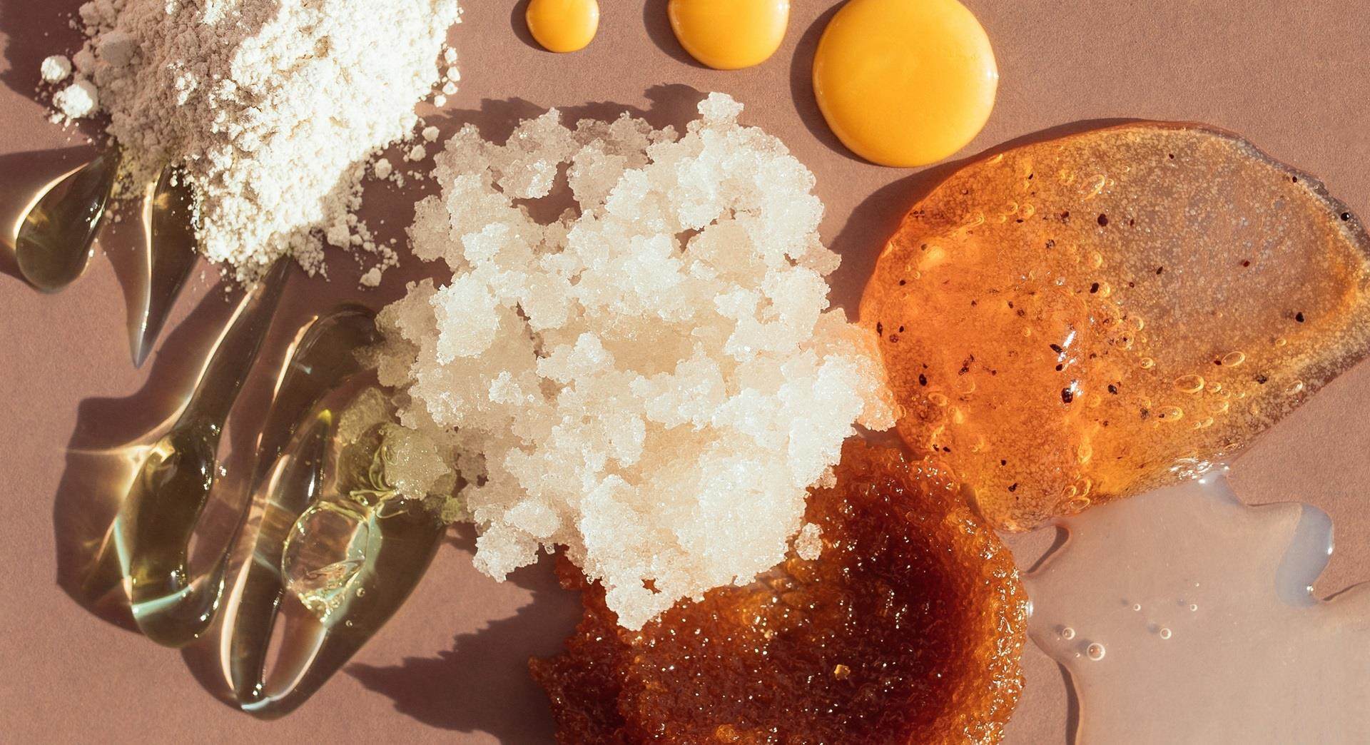 A mixture of differently textured cosmetic formulations arranged on a pink background